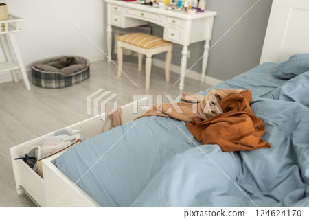 Unmade bed and scattered clothes in cozy bedroom interior. Conveys daily clutter, household disorder, and the reality of a messy lived-in home. Unmade bed and scattered clothes in cozy bedroom interior. Conveys daily clutter, household disorder, and the reality of a messy lived-in home. 124624170