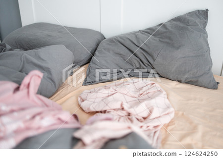 Unmade bed with wrinkled pillows and scattered clothes. Domestic mess and an untidy living space in everyday life. 124624250
