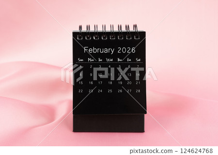 Black desk calendar for February 2026 on a pink color silk textile. 124624768