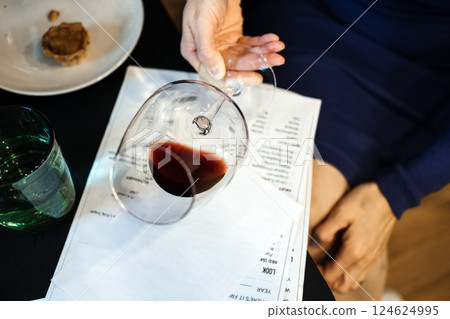 Wine glass tilted over tasting notes at a fine dining table. Curated experiences, sensory design, sommelier culture 124624995