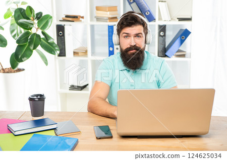 Serious man listening to webinar in headphones using laptop in office, online education 124625034