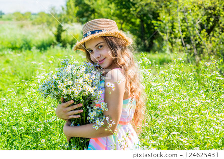 Happy little kid wear sun hat on long wavy hair holding beautiful chamomile flowers spa and beauty care on sunny summer landscape, look Happy little kid wear sun hat on long wavy hair holding beautiful chamomile flowers spa and beauty care on sunny summer landscape, look 124625431