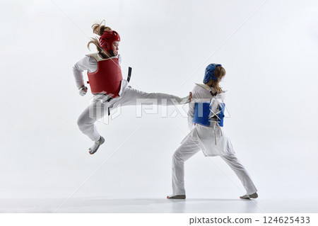 Two female taekwondo fighters crossing high kicks in mirrored motion, training against white background. 124625433
