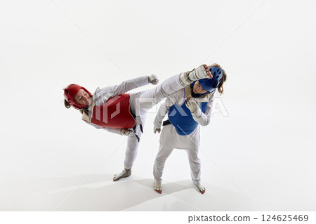 Red fighter executing spinning kick to head of blue opponent in technical combat maneuver, women training on white background. 124625469
