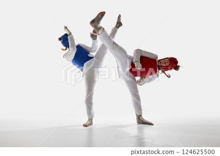 Two female taekwondo athletes in motion, fighting in synchronized kicks against white studio background. Two female taekwondo athletes in motion, fighting in synchronized kicks against white studio background. 124625500