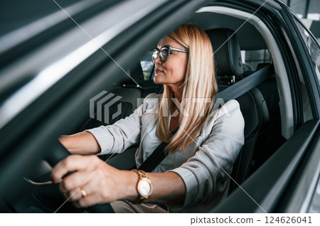 Sitting inside of the new automobile. Woman in white formal clothes is in the car dealership Sitting inside of the new automobile. Woman in white formal clothes is in the car dealership 124626041