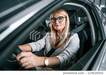 Sitting inside of the new automobile. Woman in white formal clothes is in the car dealership Sitting inside of the new automobile. Woman in white formal clothes is in the car dealership 124626042