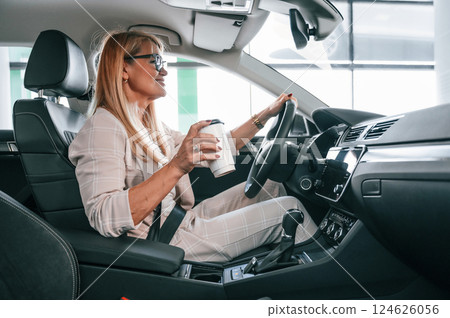 Sitting in the automobile. Woman in white formal clothes is in the car dealership 124626056