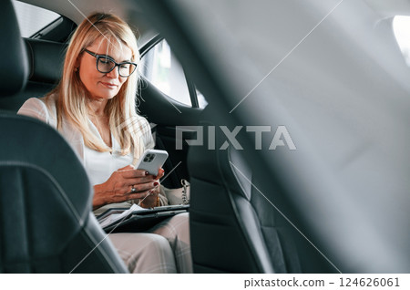 Sitting on the backseat and working. Woman in white formal clothes is in the car dealership 124626061