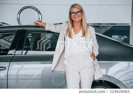 With beautiful new automobile. Woman in white formal clothes is in the car dealership With beautiful new automobile. Woman in white formal clothes is in the car dealership 124626063