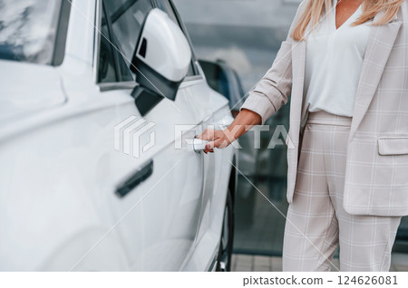 Close up view of hand opening the door. Woman in white formal clothes is in the car dealership Close up view of hand opening the door. Woman in white formal clothes is in the car dealership 124626081