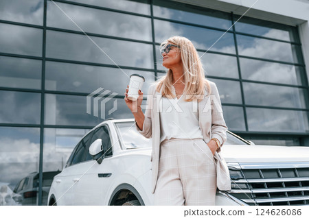 Standing outdoors near new automobile. Woman in white formal clothes is in the car dealership 124626086