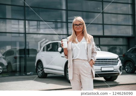 Enjoying fresh drink. Woman in white formal clothes is in the car dealership Enjoying fresh drink. Woman in white formal clothes is in the car dealership 124626090