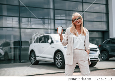 Enjoying fresh drink. Woman in white formal clothes is in the car dealership 124626093