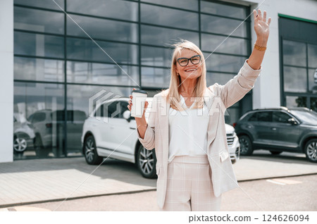 Talking to someone. Woman in white formal clothes is in the car dealership 124626094