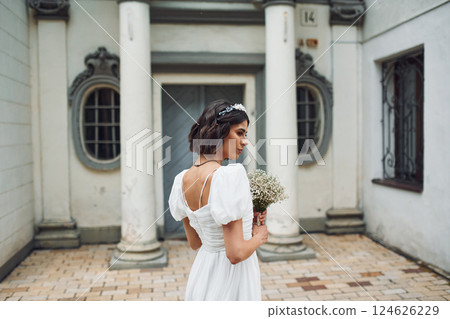 Rear view. Holding flowers. Bride in dress is outdoors before her wedding begins 124626229