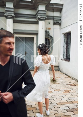 Standing against building. Beautiful bride with his fiance is celebrating wedding outdoors 124626231