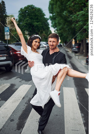Man holding his woman in hands. Beautiful bride with his fiance is celebrating wedding outdoors 124626236
