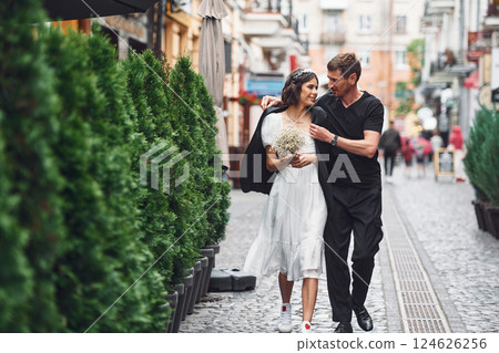 On the street with green plants on the left side. Beautiful bride with his fiance is celebrating wedding outdoors 124626256