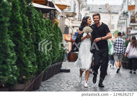 On the street with green plants on the left side. Beautiful bride with his fiance is celebrating wedding outdoors 124626257