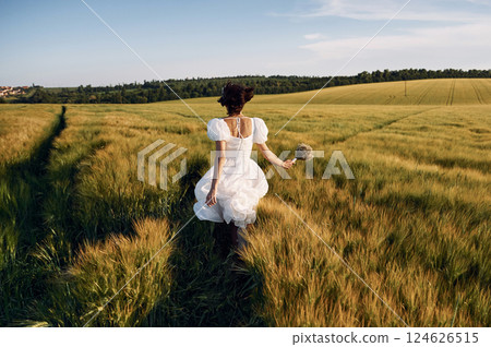 Rear view. Beautiful young bride in white dress is on the agricultural field at sunny day 124626515