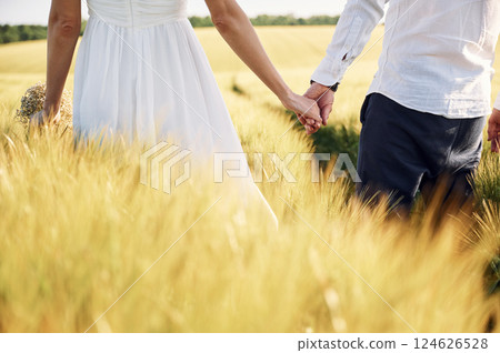 Holding each other by the hands. Couple just married. Together on the majestic agricultural field at sunny day Holding each other by the hands. Couple just married. Together on the majestic agricultural field at sunny day 124626528