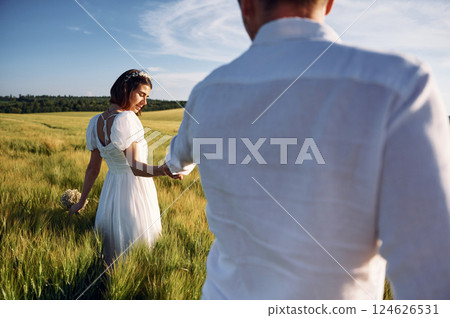 Holding each other by the hands. Couple just married. Together on the majestic agricultural field at sunny day 124626531