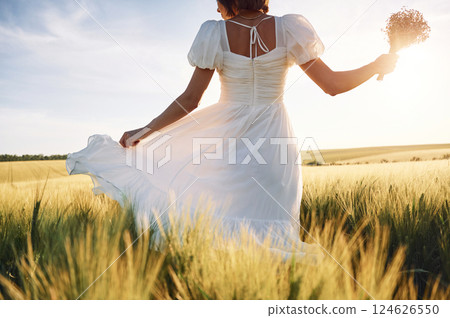 Having a walk. Beautiful young bride in white dress is on the agricultural field at sunny day 124626550