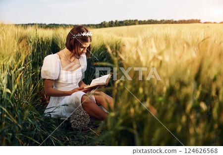 With book. Beautiful young bride in white dress is on the agricultural field at sunny day 124626568