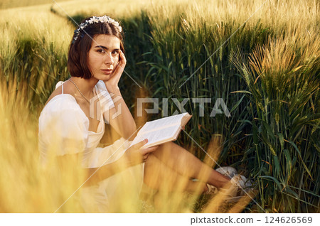With book. Beautiful young bride in white dress is on the agricultural field at sunny day 124626569