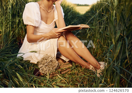 With book. Beautiful young bride in white dress is on the agricultural field at sunny day 124626570