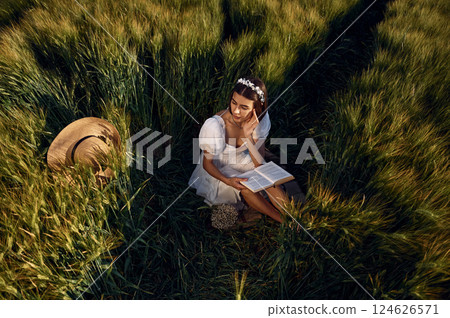With book. Beautiful young bride in white dress is on the agricultural field at sunny day 124626571
