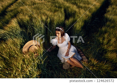 With book. Beautiful young bride in white dress is on the agricultural field at sunny day 124626572
