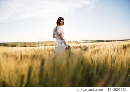 Enjoying the nature. Beautiful young bride in white dress is on the agricultural field at sunny day 124626581