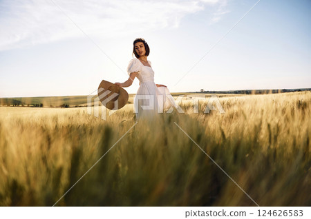 Enjoying the nature. Beautiful young bride in white dress is on the agricultural field at sunny day 124626583