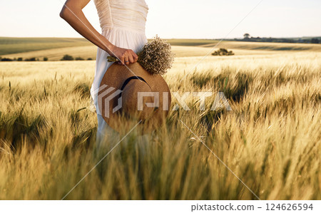 Cropped view. Holding hat in hand. Beautiful young bride in white dress is on the agricultural field at sunny day 124626594