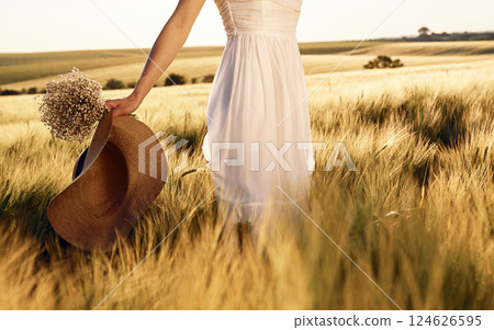 Cropped view. Holding hat in hand. Beautiful young bride in white dress is on the agricultural field at sunny day 124626595