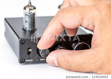 Focused image of a person adjusting the bass knob on a black amplifier. 124626805