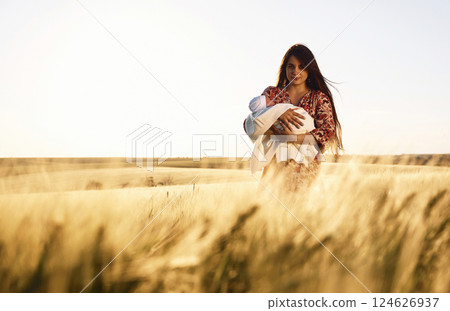 Front view. Gorgeous woman is on the agricultural field with her newborn baby 124626937