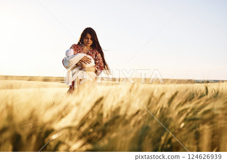 Front view. Gorgeous woman is on the agricultural field with her newborn baby 124626939
