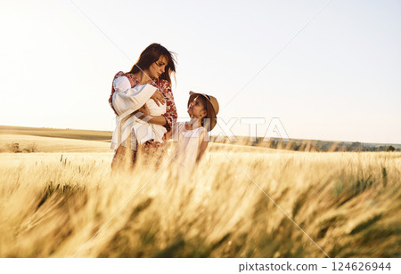 Standing together. Mother with her newborn baby and girl is on the field at sunny day 124626944