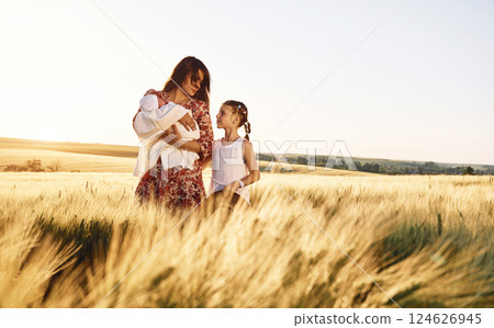 Standing together. Mother with her newborn baby and girl is on the field at sunny day Standing together. Mother with her newborn baby and girl is on the field at sunny day 124626945