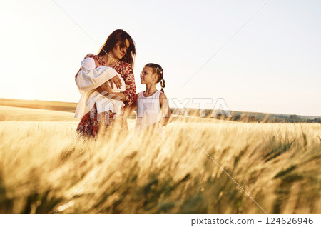 Standing together. Mother with her newborn baby and girl is on the field at sunny day 124626946