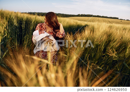 Sitting on the ground. Gorgeous woman is on the agricultural field with her newborn baby Sitting on the ground. Gorgeous woman is on the agricultural field with her newborn baby 124626950