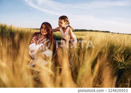 Woman is sitting on the ground. Mother with her newborn baby and girl is on the field at sunny day together 124626953