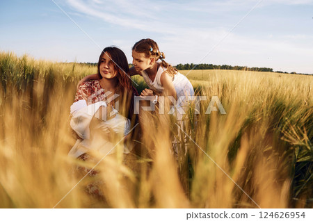 Woman is sitting on the ground. Mother with her newborn baby and girl is on the field at sunny day together Woman is sitting on the ground. Mother with her newborn baby and girl is on the field at sunny day together 124626954