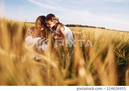 Woman is sitting on the ground. Mother with her newborn baby and girl is on the field at sunny day together Woman is sitting on the ground. Mother with her newborn baby and girl is on the field at sunny day together 124626955
