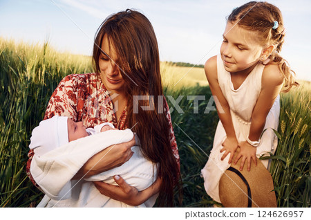 Looking at the newborn baby. Mother with girl is on the field at sunny day together Looking at the newborn baby. Mother with girl is on the field at sunny day together 124626957