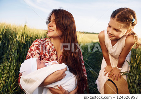 Looking at the newborn baby. Mother with girl is on the field at sunny day together 124626958