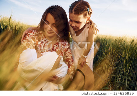 Looking at the newborn baby. Mother with girl is on the field at sunny day together 124626959
